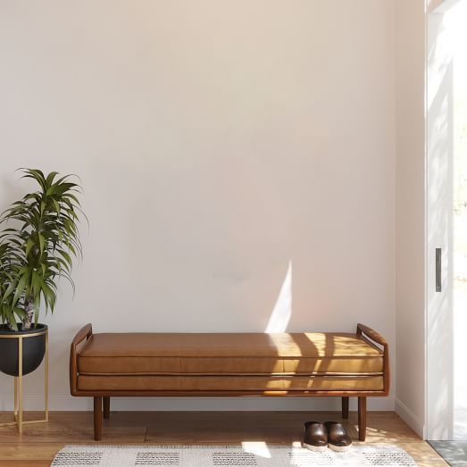 a brown bench sitting next to a potted plant on top of a wooden floor