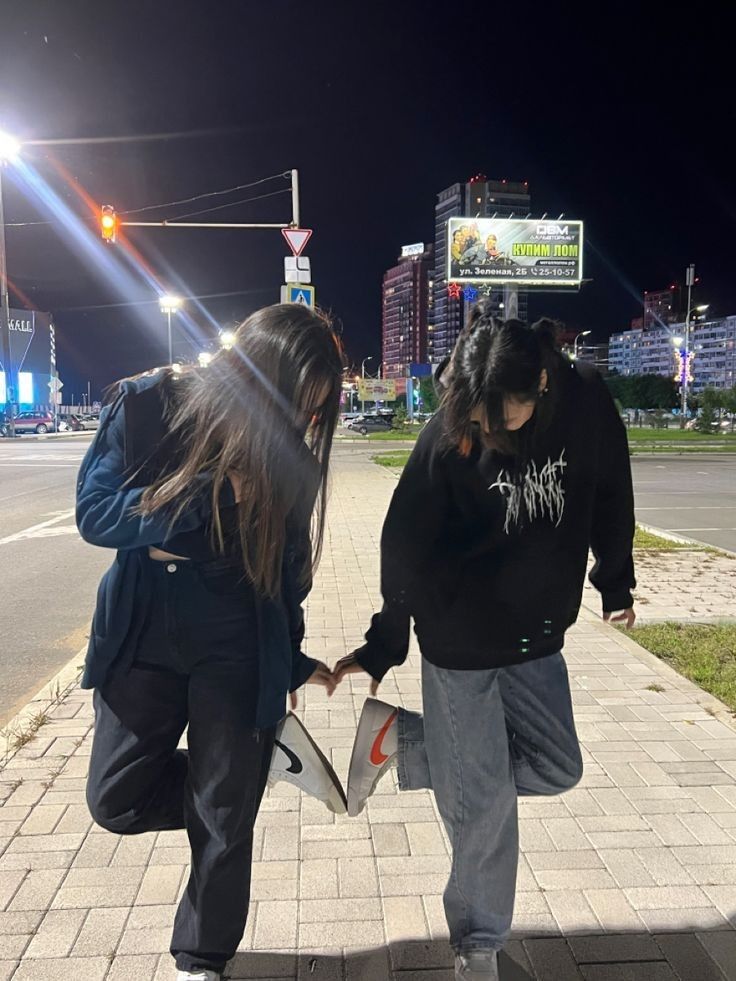 two people are walking down the sidewalk at night with their hands in each other's pockets