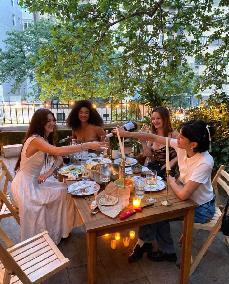 a group of women sitting around a wooden table with plates and glasses on top of it