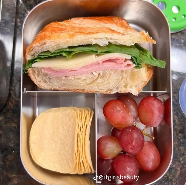 a sandwich in a metal tray with grapes and crackers