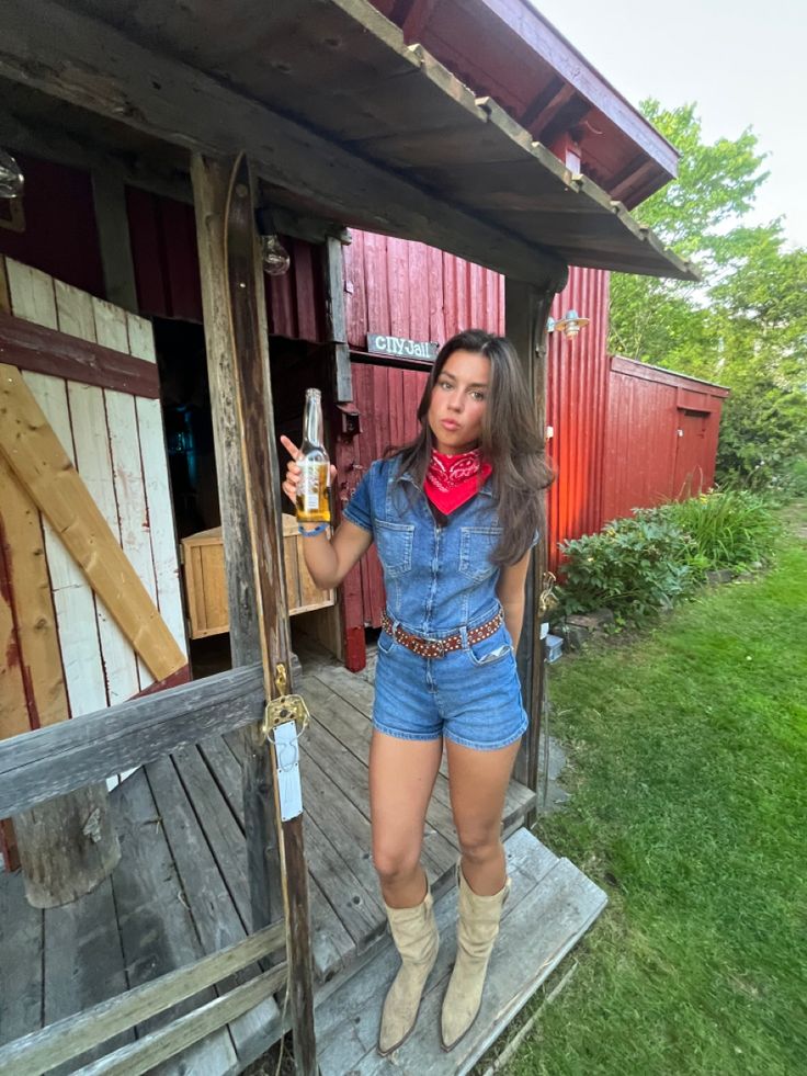 a woman in short shorts and cowboy boots standing on the porch of a red barn