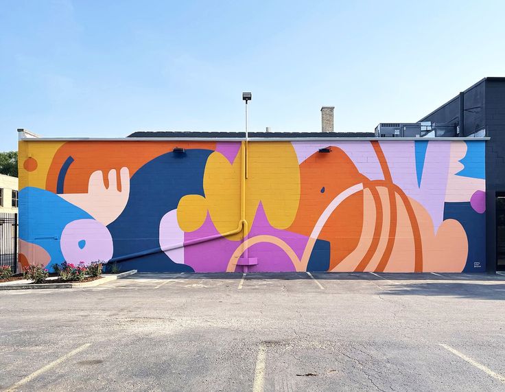 an empty parking lot in front of a building with a colorful mural on it's side