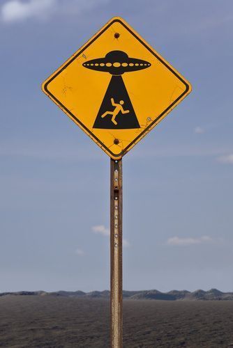 a yellow sign that is on top of a pole in the grass with mountains in the background