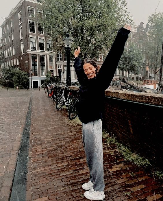 a woman standing on top of a brick road holding her arms up in the air