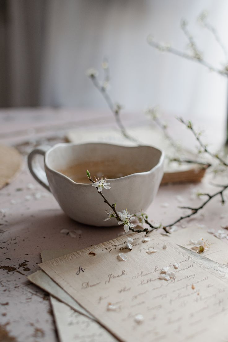 a white bowl sitting on top of a table next to papers and flowers in it