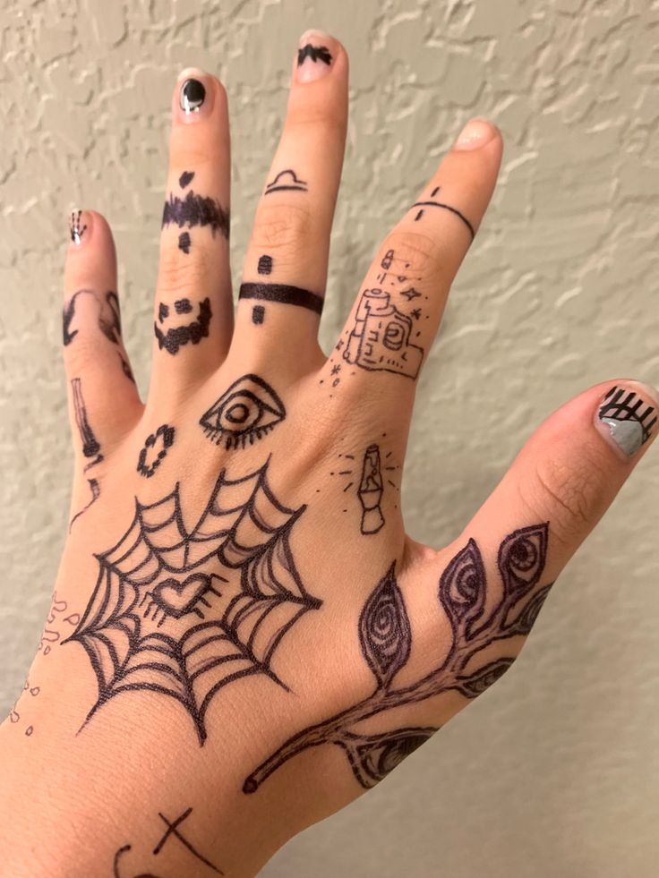 A hand with various doodles on it; including a heart-shaped spider web, a plant with eyes on the leaves, simple lava lamp and gun designs, and bands of different patterns on the fingers. Sharpie Hand Doodles, Doodles To Draw On Your Hand, Sharpie Doodles, Grunge Tattoo, Pretty Hand Tattoos, Finger Tattoo Designs, Sharpie Tattoos, Pen Tattoo, Hand Doodles