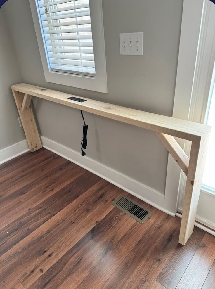 a wooden bench sitting on top of a hard wood floor next to a window with blinds