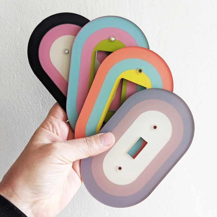 a hand is holding some colorful magnets in front of a white wall with a light switch on it