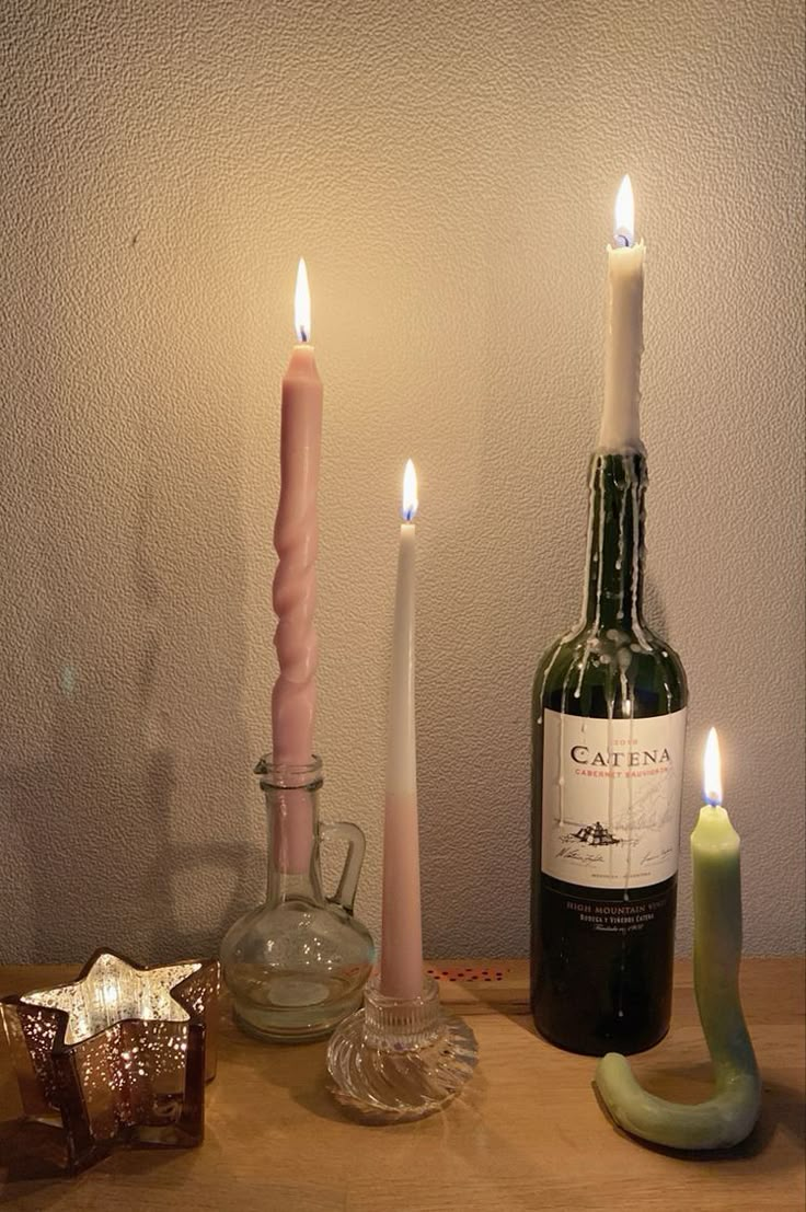 two candles are lit next to a bottle of wine and a candle holder on a table