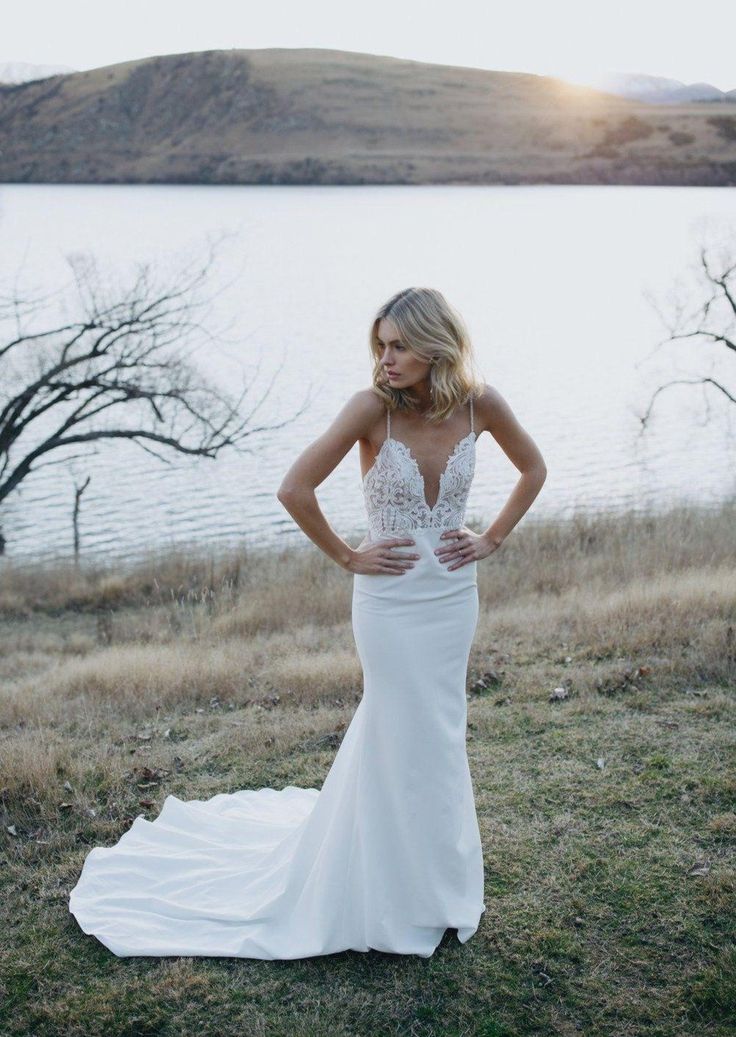 a woman in a white wedding dress standing on the grass next to a body of water