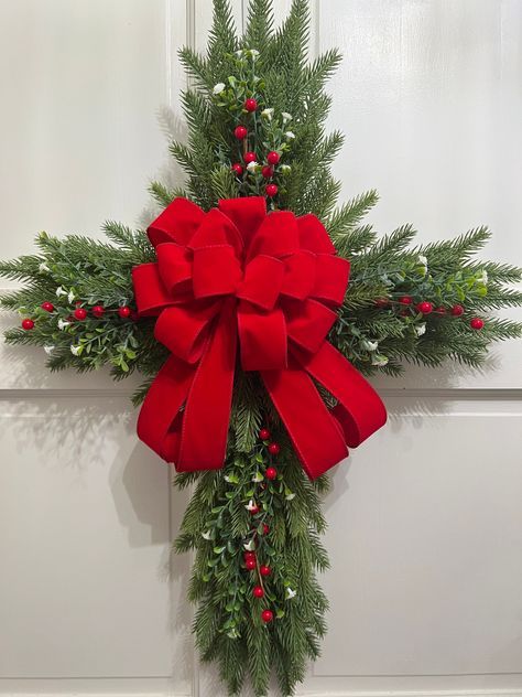 a cross decorated with holly and red bow hanging from the side of a building door