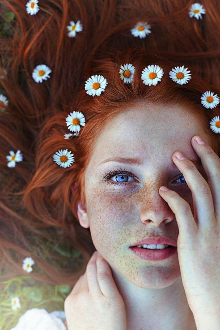 a woman with red hair and daisies on her head is laying in the grass