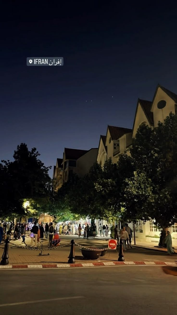 people are standing on the sidewalk in front of some houses at night with bright lights