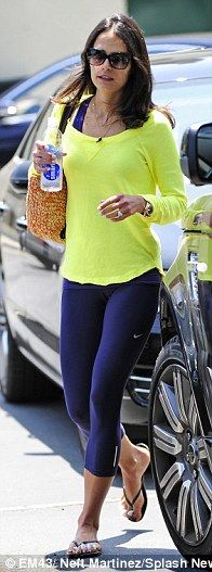 a woman in yellow shirt and blue leggings walking next to a car with a bicycle