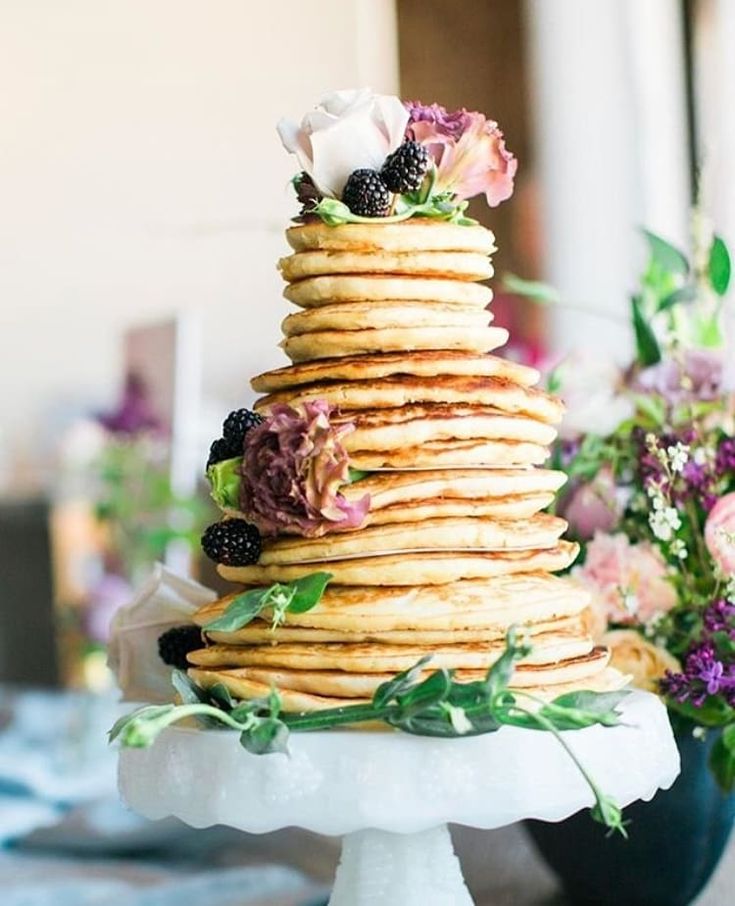 a stack of pancakes sitting on top of a table next to flowers and greenery