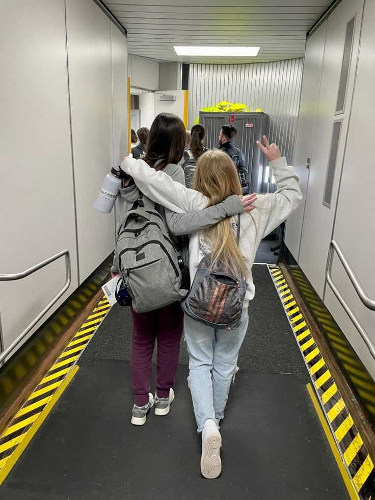 two girls walking down a hallway with their backs to each other and backpacks on