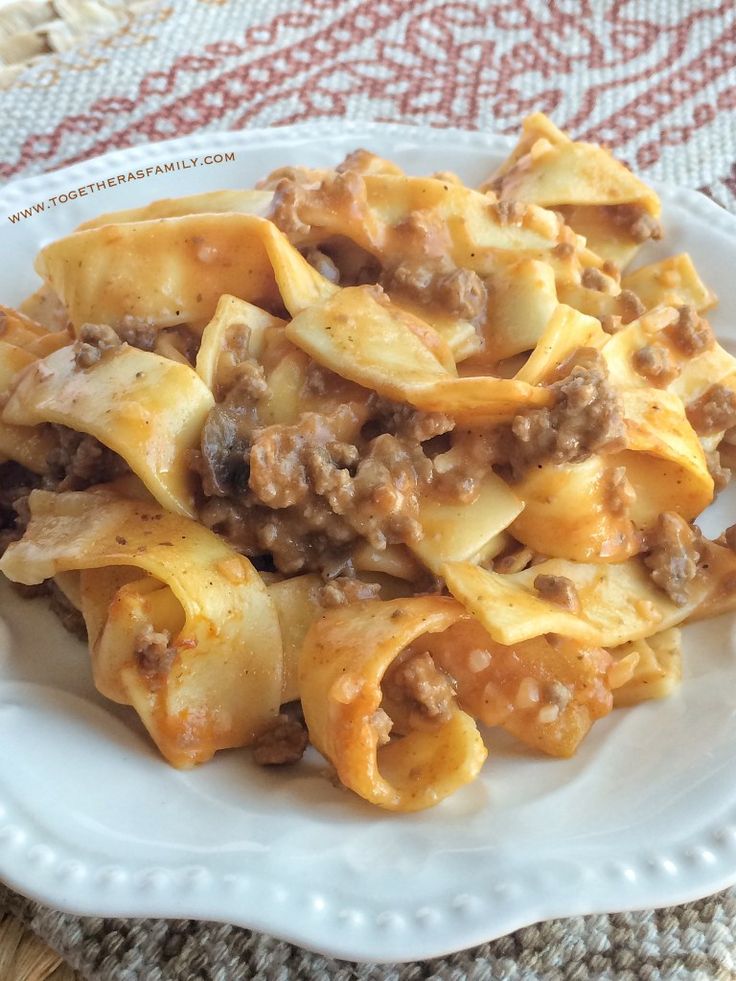 a white plate topped with pasta and meat covered in sauce on top of a table