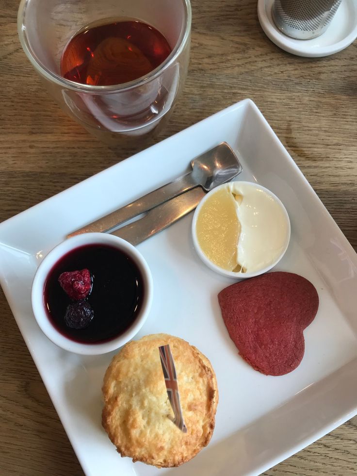 a white plate topped with desserts next to cups of tea and silverware on top of a wooden table