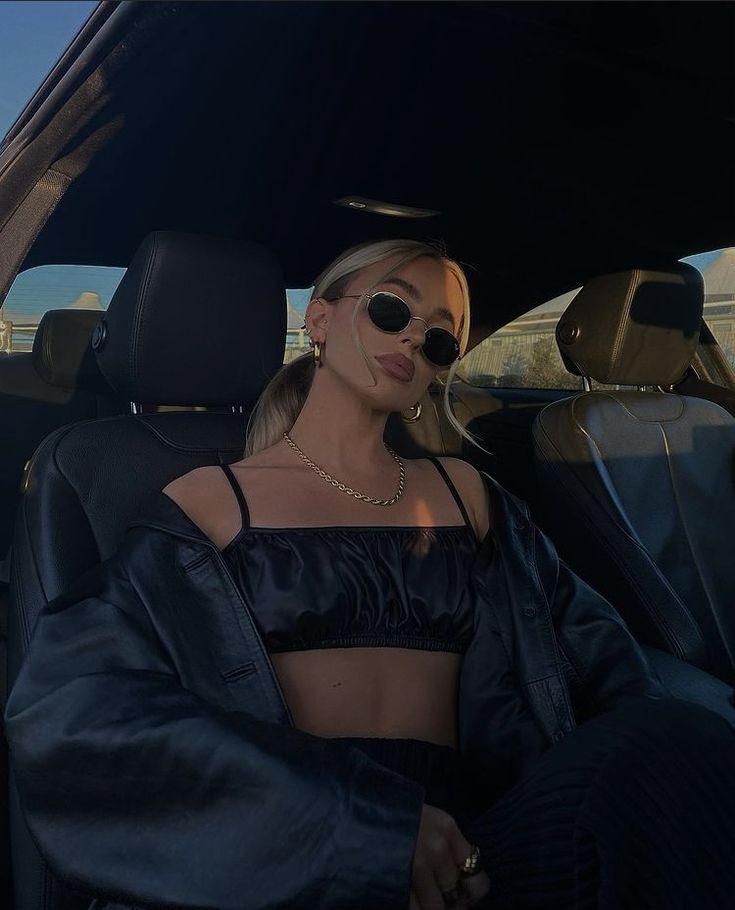 a woman sitting in the back seat of a car wearing sunglasses and a crop top