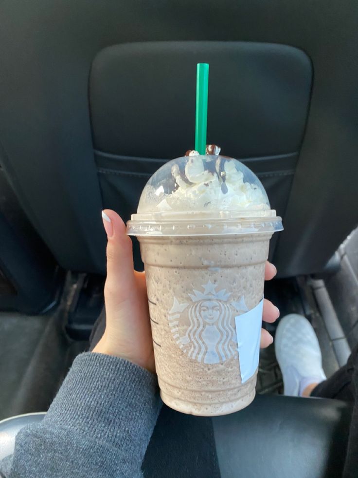 a person holding up a starbucks drink in their hand while sitting in the back seat of a car