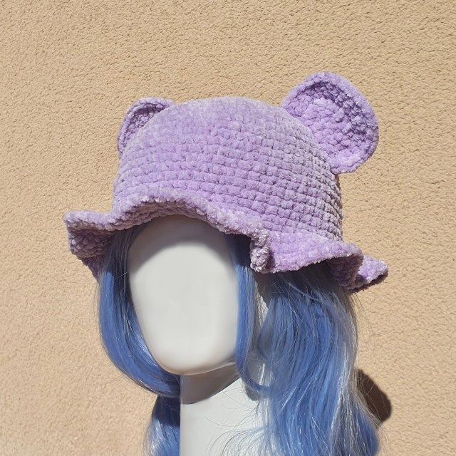 a wig with blue hair wearing a purple crochet bear hat on top of it