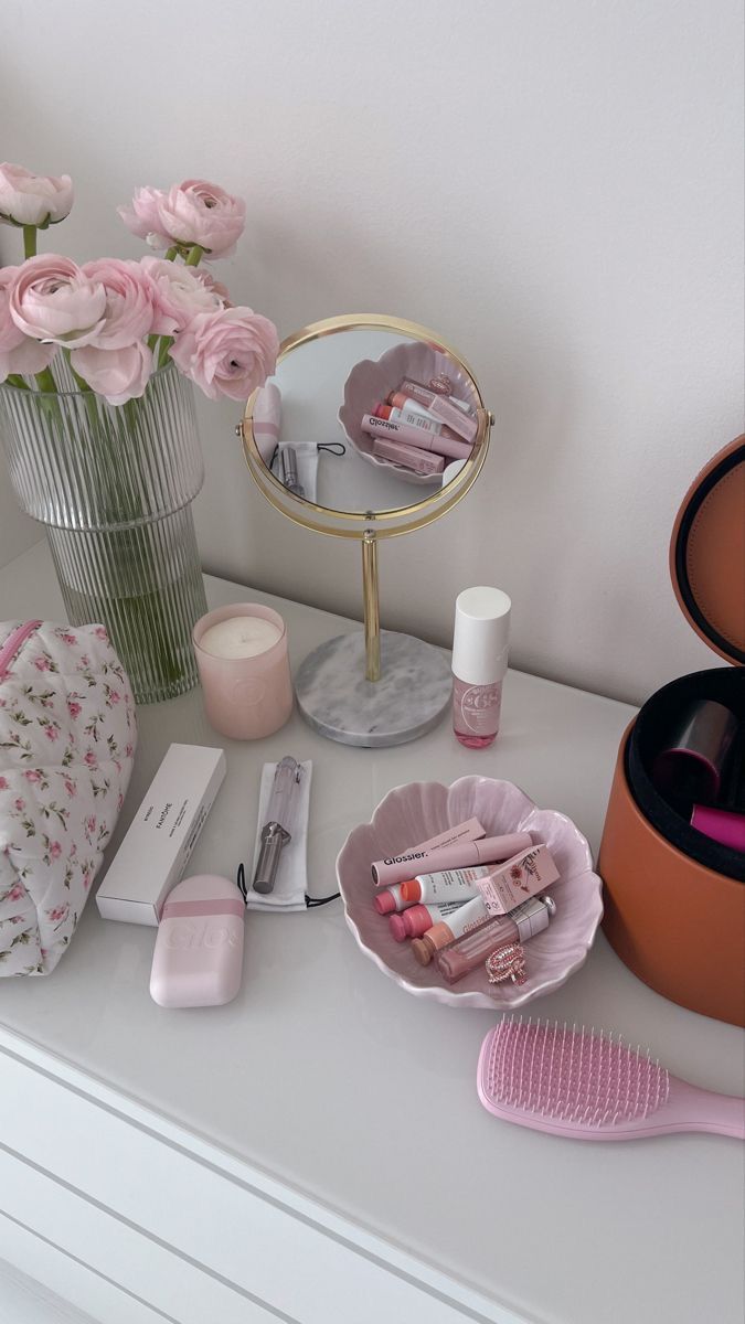 a white dresser topped with lots of pink flowers and makeup items next to a mirror