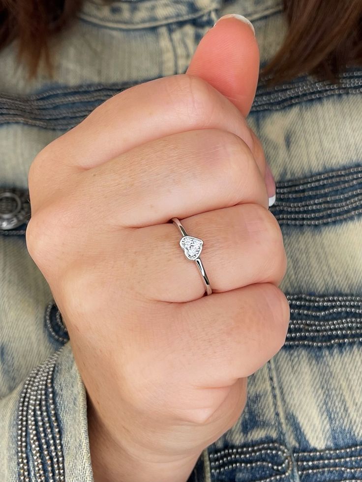 a woman's hand with a diamond ring on her finger, wearing a denim jacket