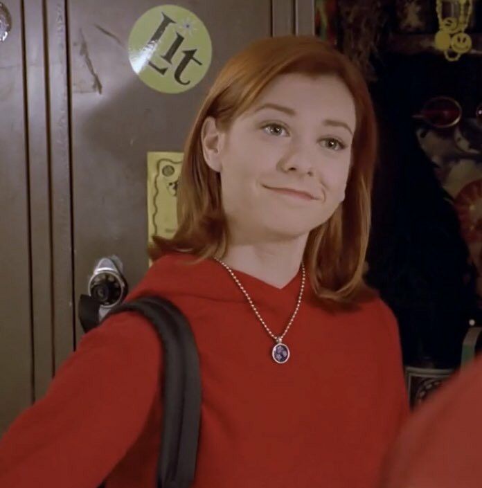 a woman wearing a red shirt and carrying a black backpack in front of a door