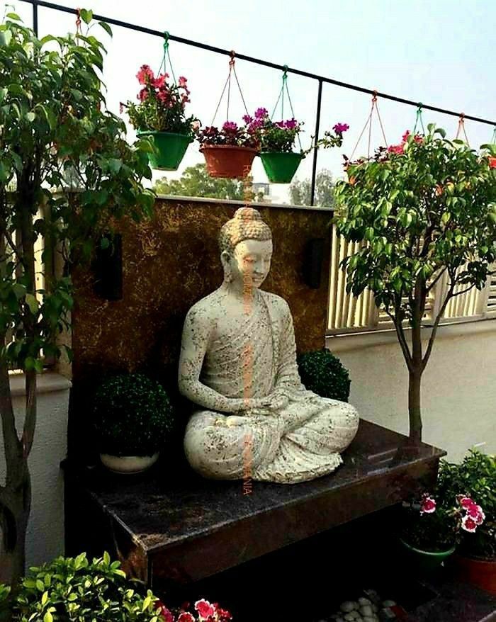 a buddha statue sitting on top of a wooden bench surrounded by potted plants and flowers