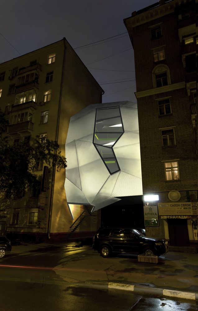 a large white structure sitting on the side of a road next to tall buildings at night