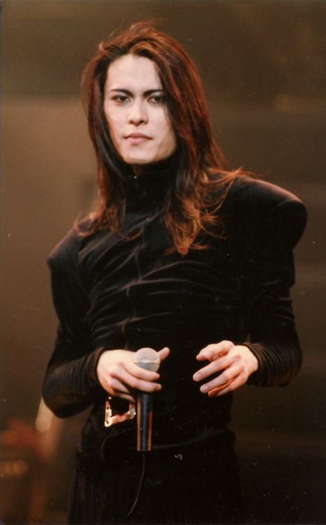 a woman with long hair holding a microphone in front of her chest and wearing a black dress