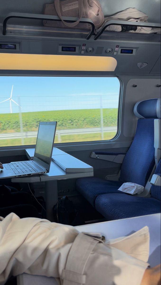 a laptop computer sitting on top of a desk next to a window with wind turbines in the background