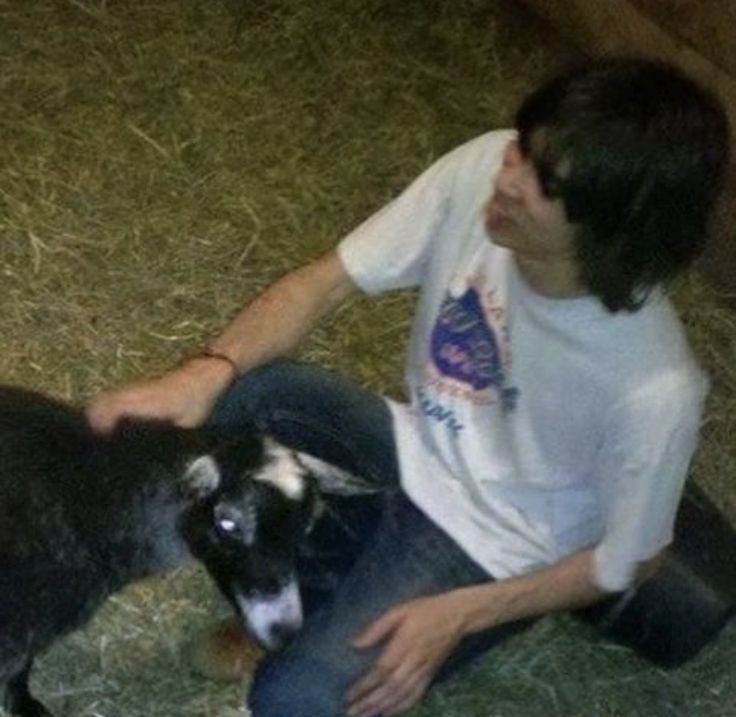 a man sitting on the ground petting a small black and white goat with its mouth open