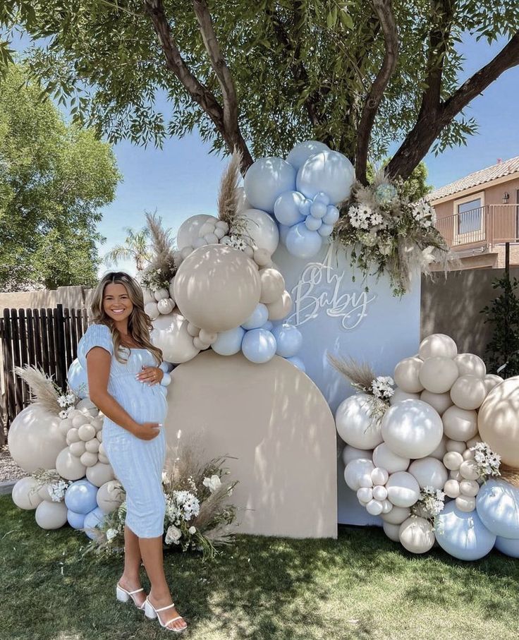 a woman standing in front of a sign with balloons and flowers on it that says my baby