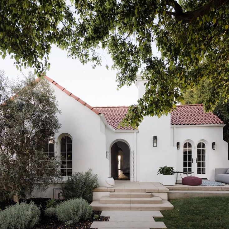 a white house with steps leading up to the front door and patio area, surrounded by trees