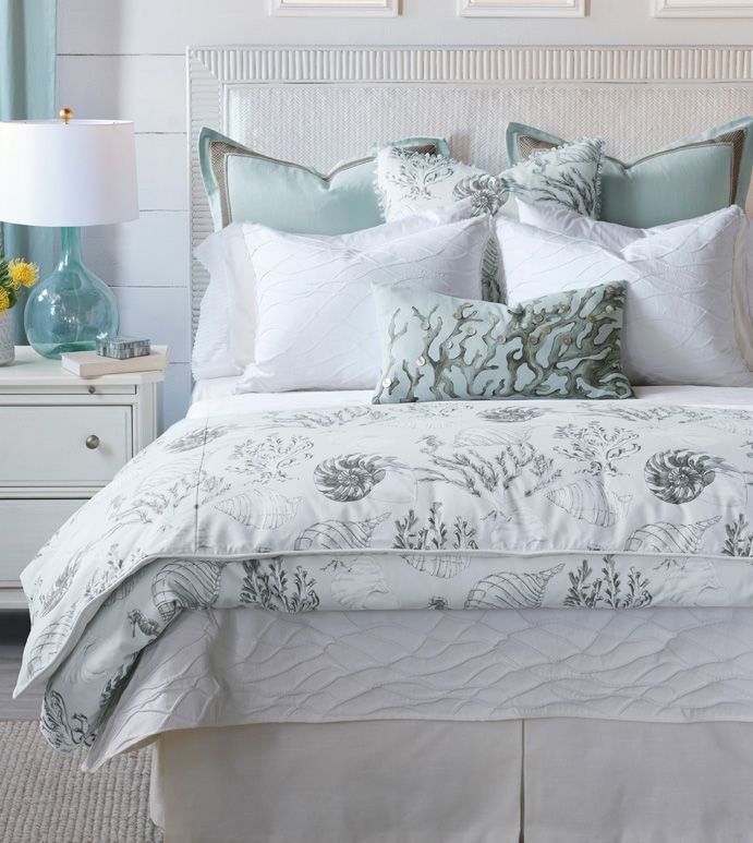 a bed with white and blue comforters in a bedroom next to a lamp on a dresser