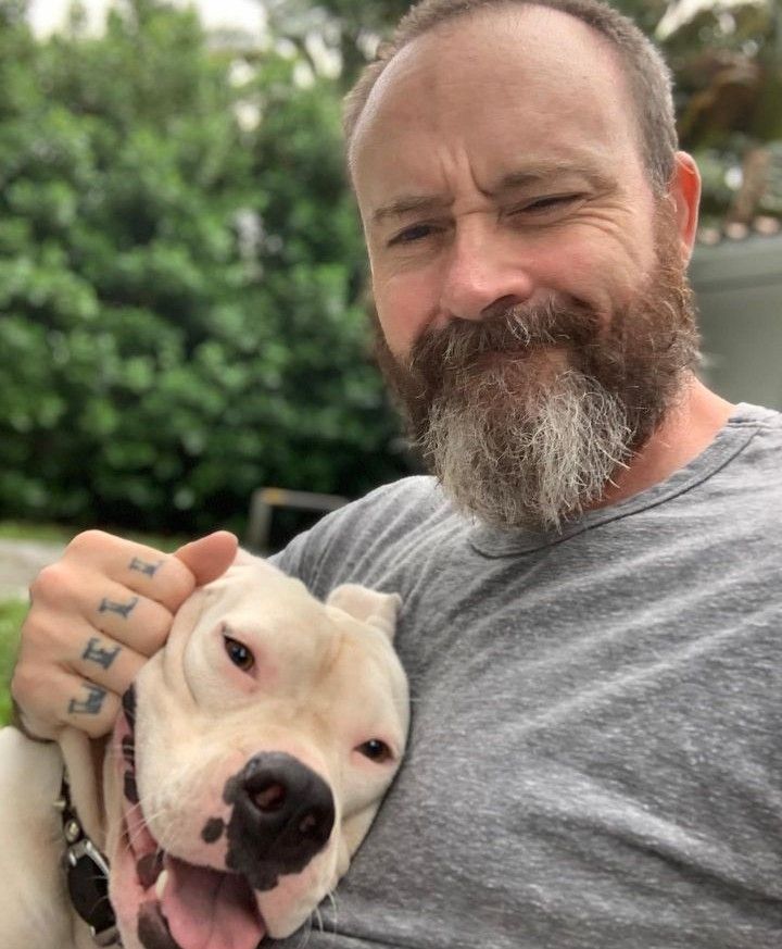 a man holding a white dog in his arms with tattoos on it's chest