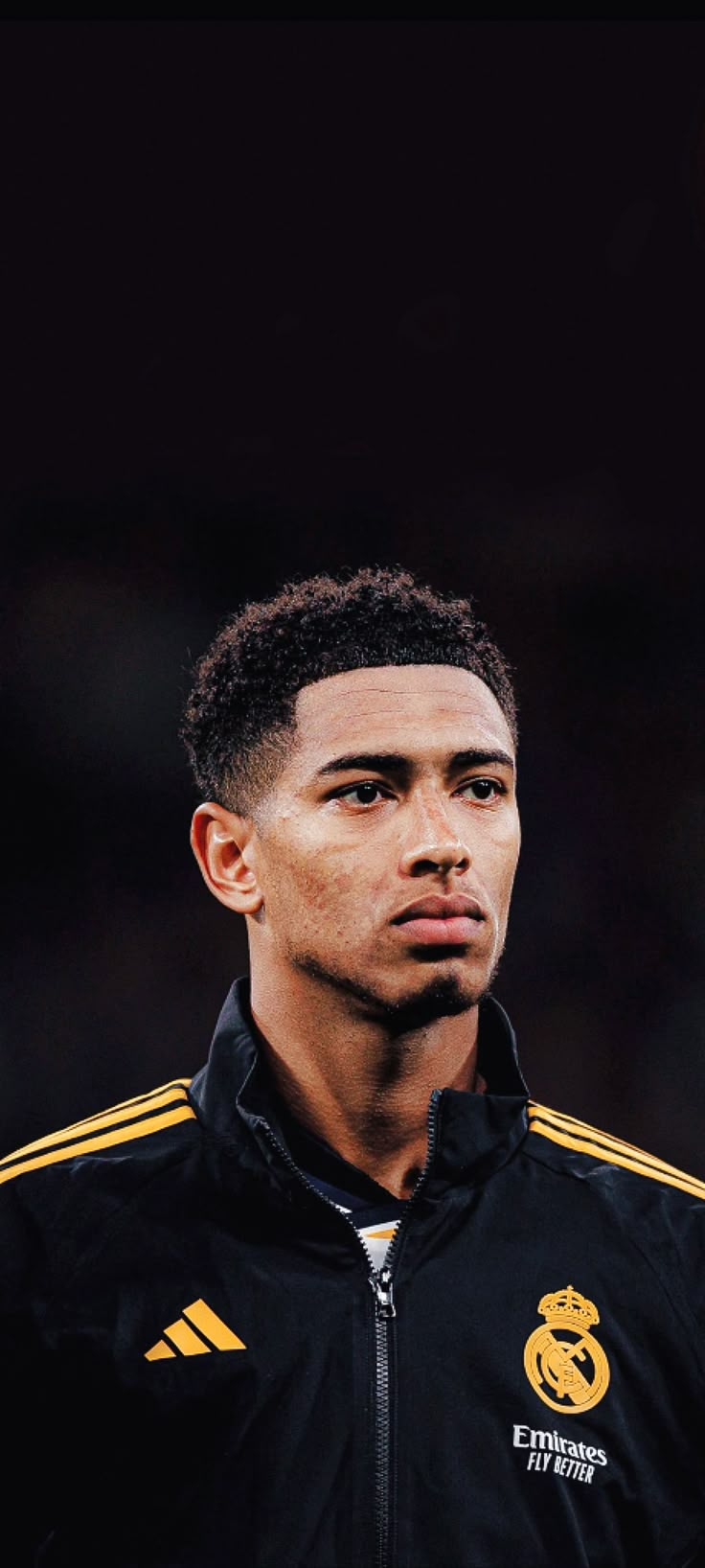 a close up of a person wearing a black and yellow jacket with a soccer ball in the background