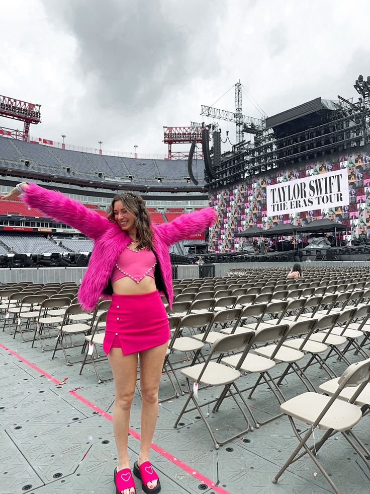 a woman standing in front of a stadium with her arms outstretched and legs spread out