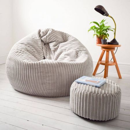 a bean bag chair and foot stool with a plant in the corner next to it