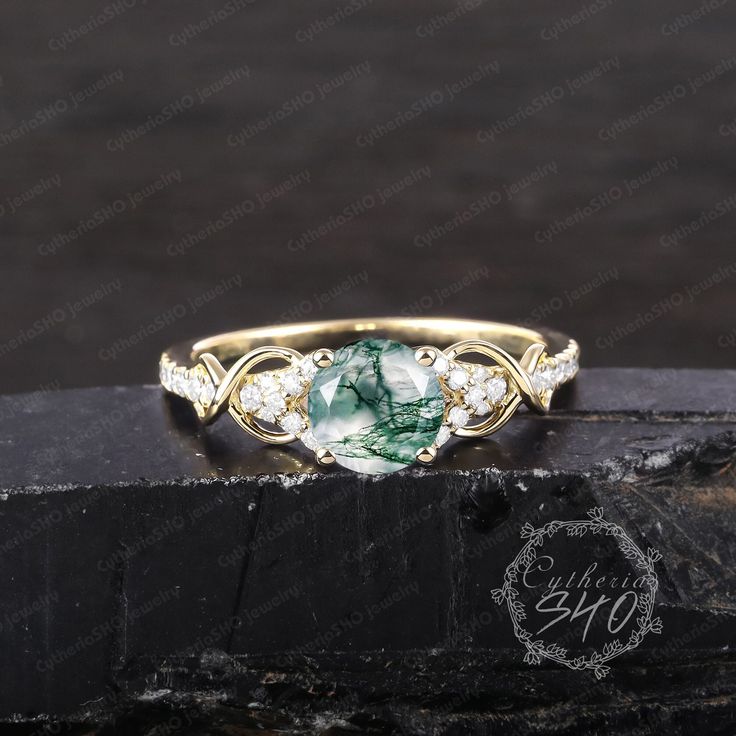 a gold ring with green and white stones on the side, sitting on top of a black