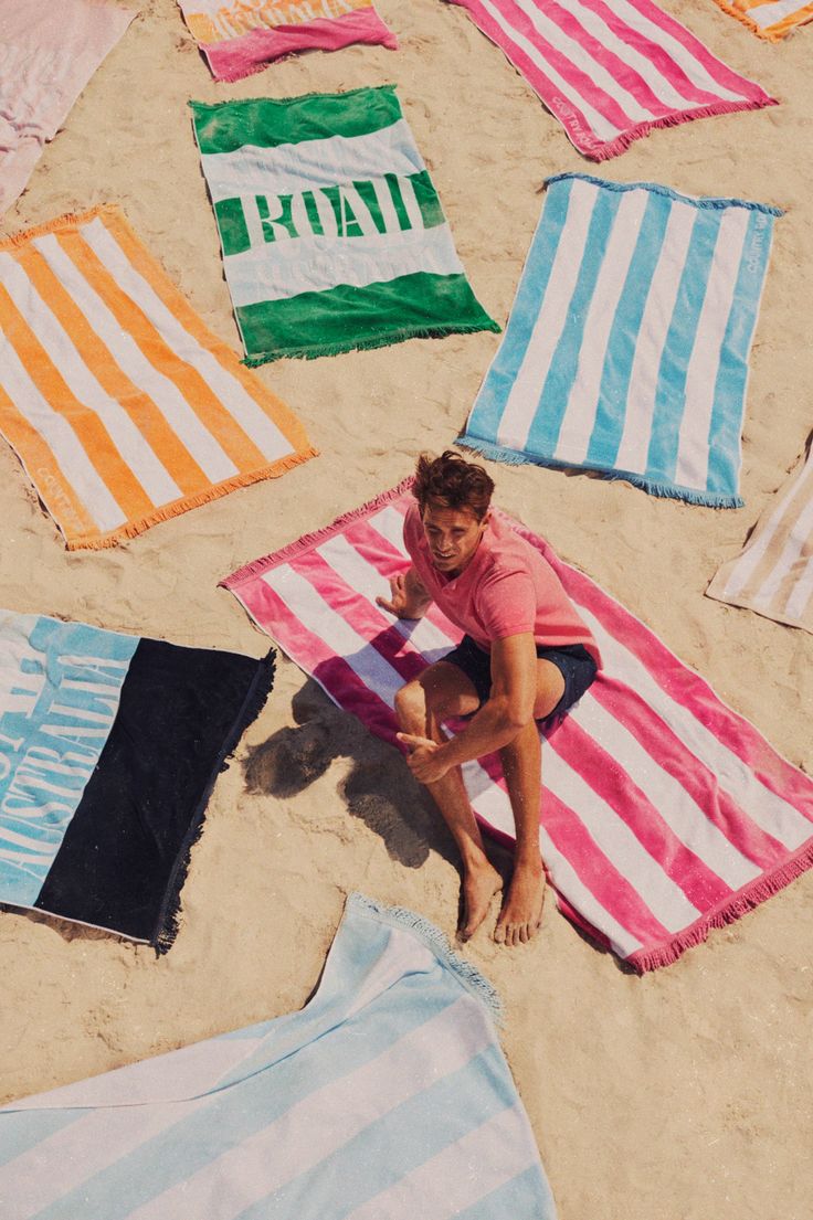 a woman sitting on top of a beach next to many blankets and towels in the sand