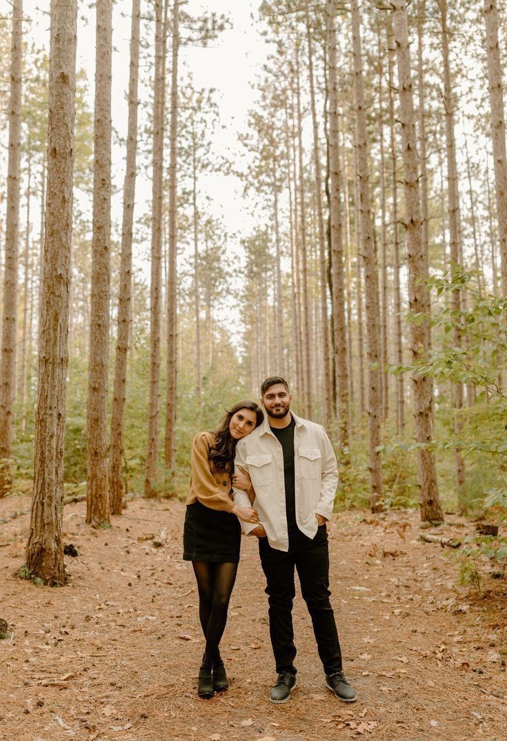 a man and woman standing in the middle of a forest