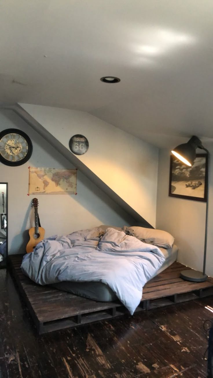 a bed sitting in the middle of a room under a slanted ceiling with clocks above it