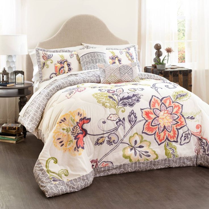 a bedroom with a bed covered in white comforter and colorful flowered bedspread