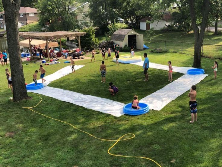 a group of people playing in a yard with an inflatable pool on the grass