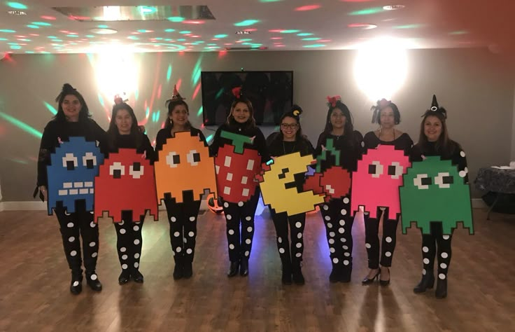 a group of people in costumes standing on a dance floor holding up paper cutouts that look like pacman