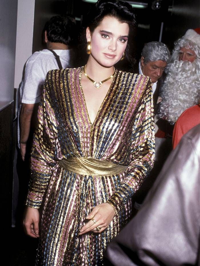 a woman wearing a gold and silver dress with santa claus in the background at an event