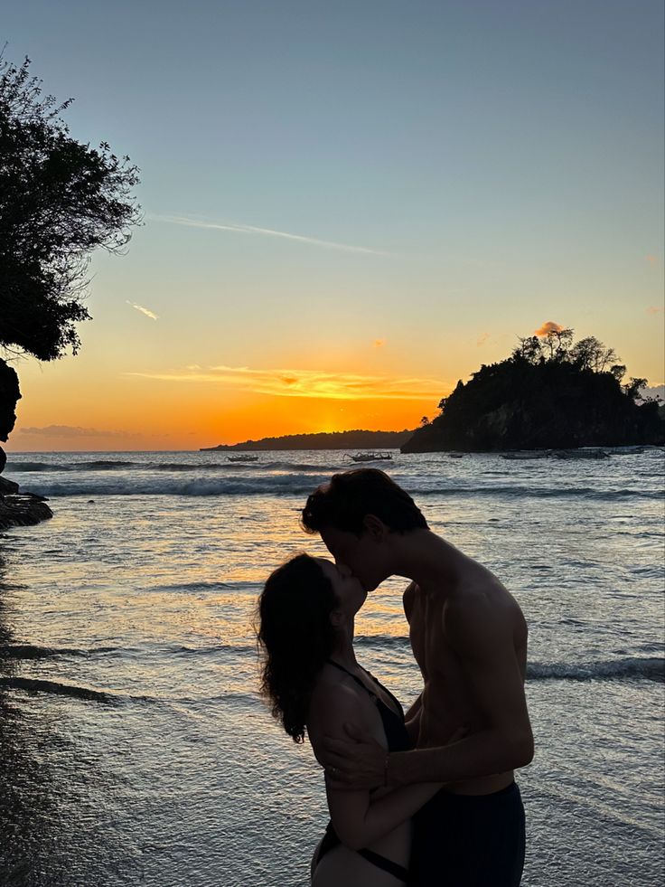 a man and woman kissing on the beach at sunset with an island in the background