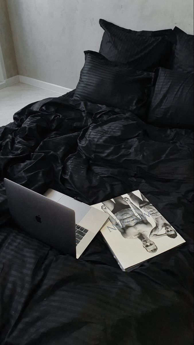 an open laptop computer sitting on top of a black bed covered in sheets and pillows